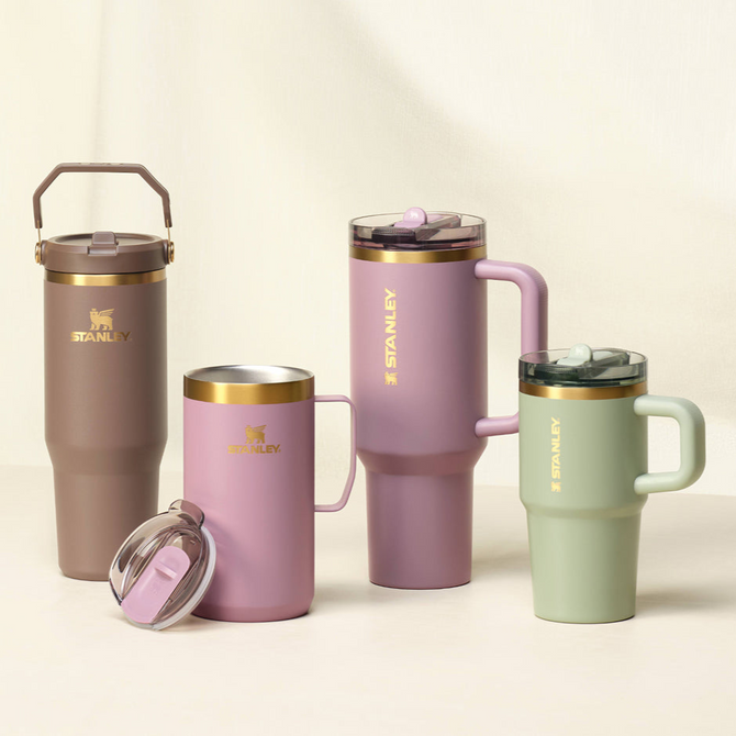 Four Stanley tumblers in pink, brown, and sage green tones with gold accents.